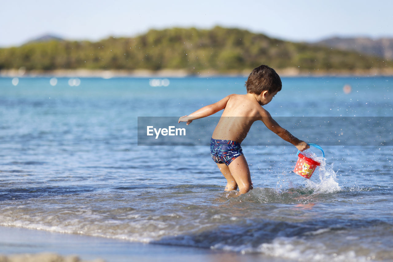 rear view of shirtless boy playing in sea