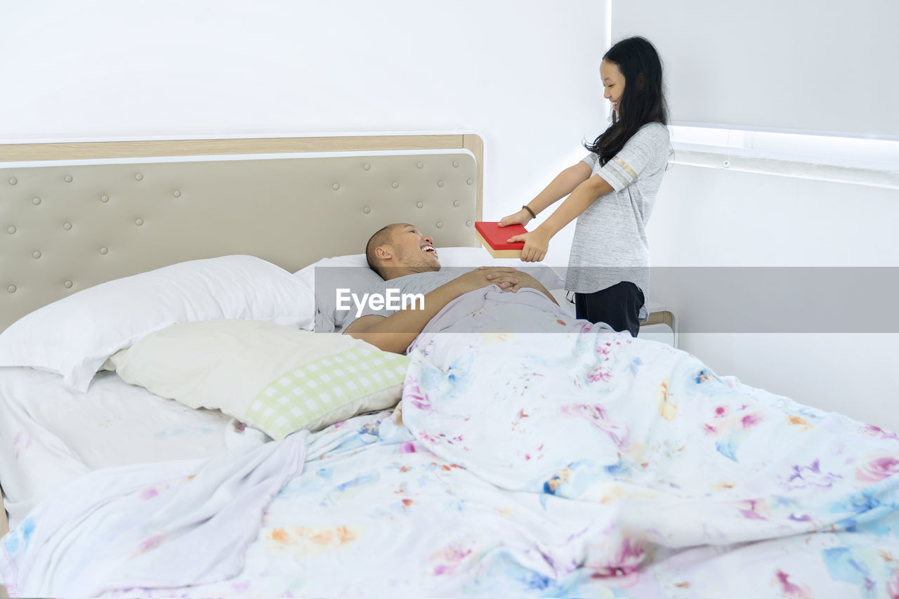 REAR VIEW OF WOMAN SITTING ON BED WITH BABY