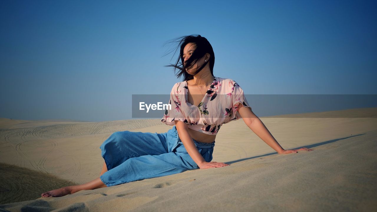 Beautiful woman sitting on sand in dessert against sky