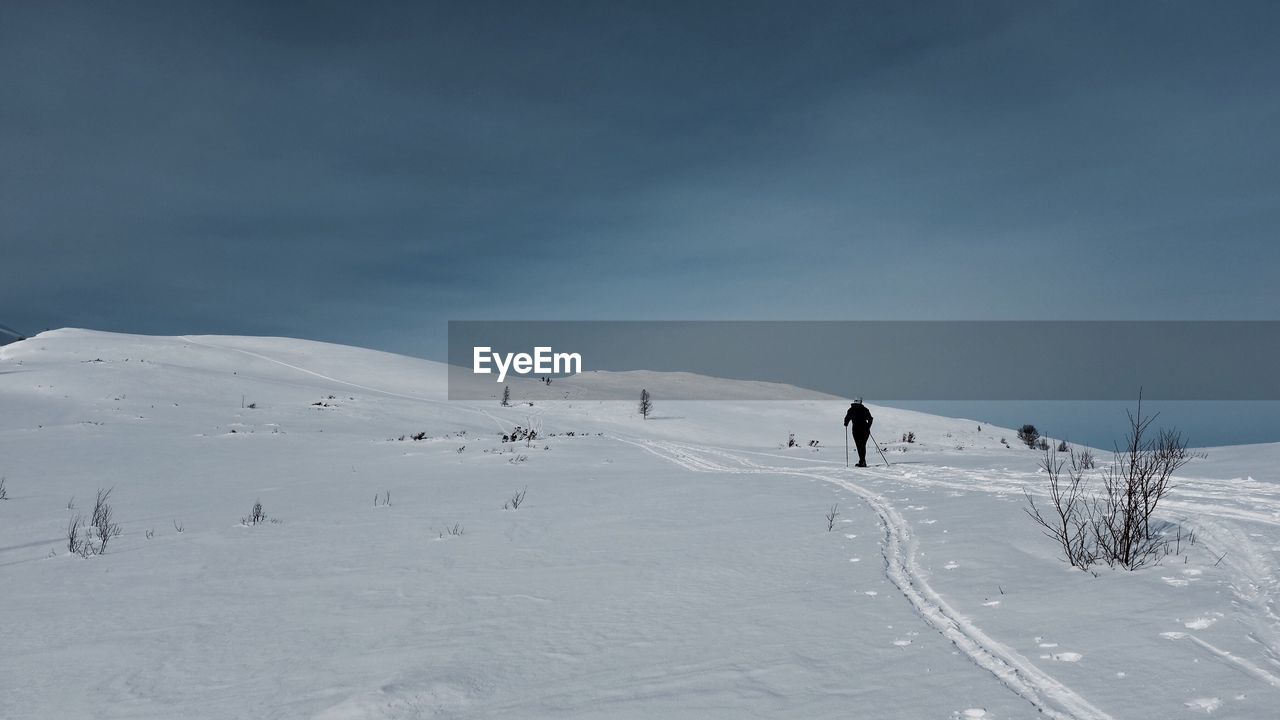 Rear view of person hiking on snow landscape against sky