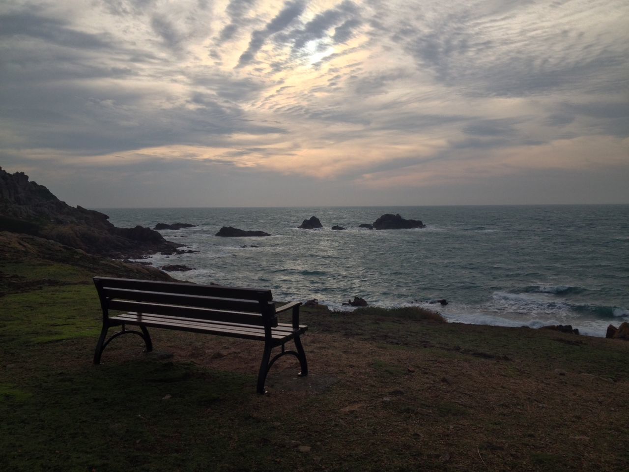 Empty bench at sea shore against cloudy sky