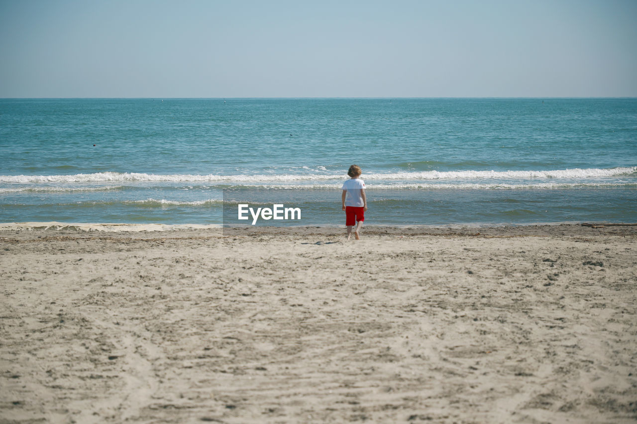 Rear view of a child standing on beach against sky