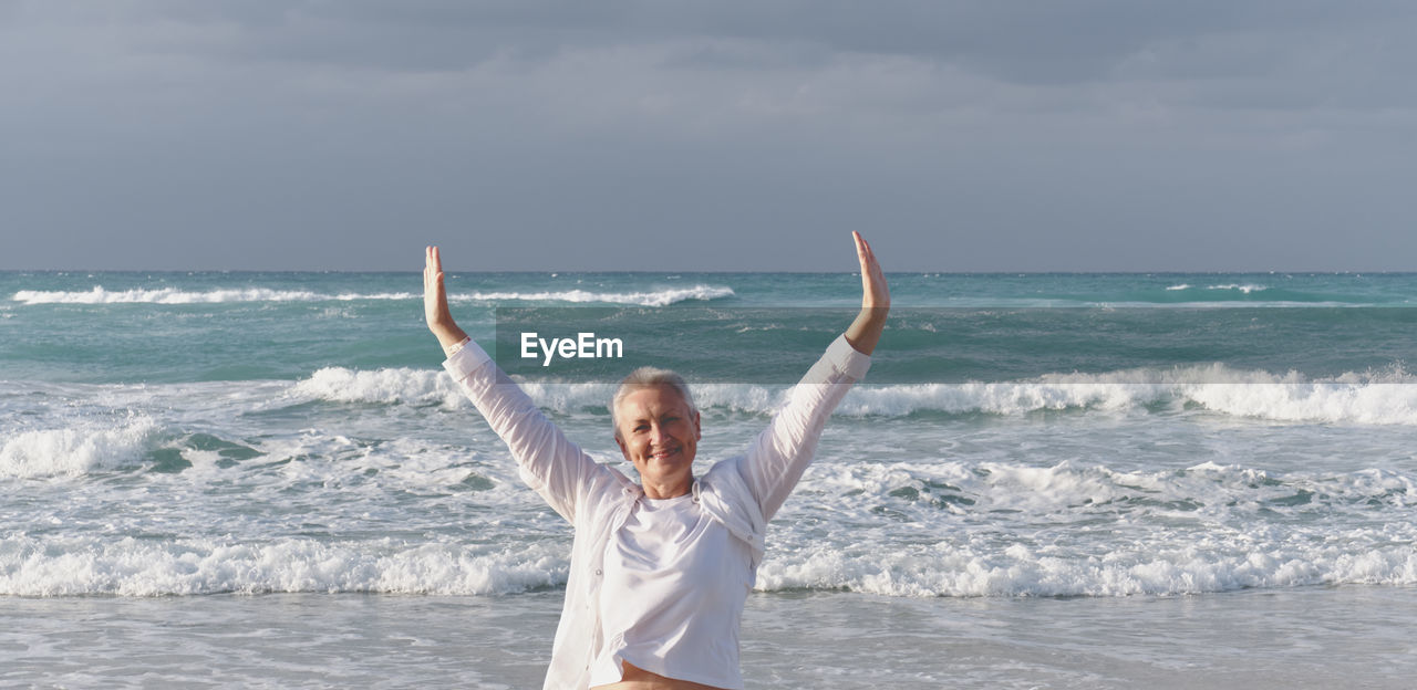 Happy smiling caucasian senior woman with outstretched arms over background of atlantic ocean, cuba.