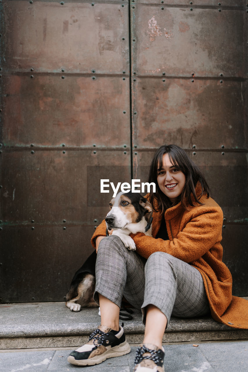 Side view of female owner gently embracing treeing walker coonhound dog while sitting on street in city