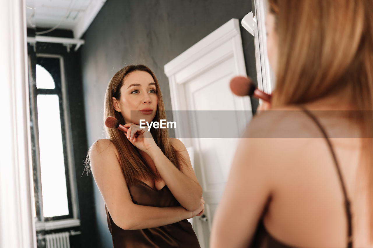 A beautiful natural woman makeup artist preens herself with makeup while looking in the mirror