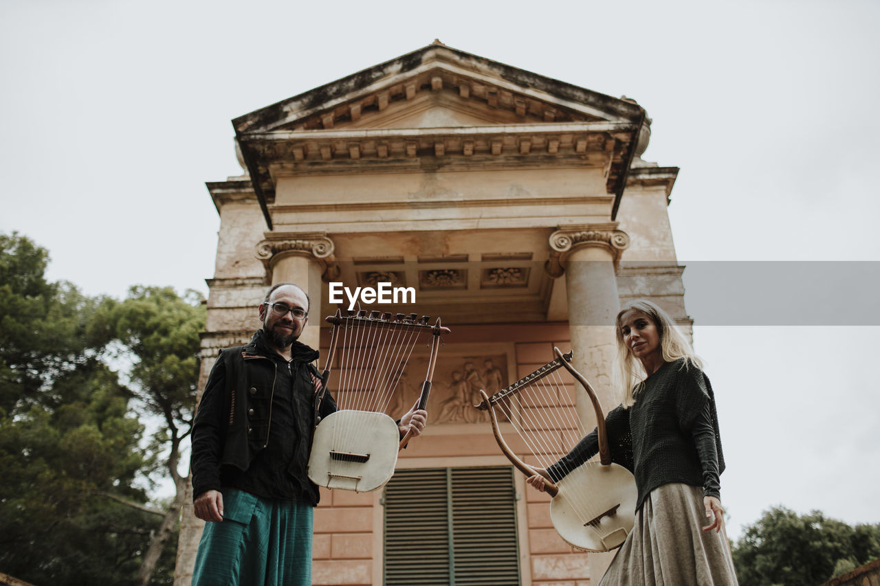 Couple holding lyra musical instrument against built structure