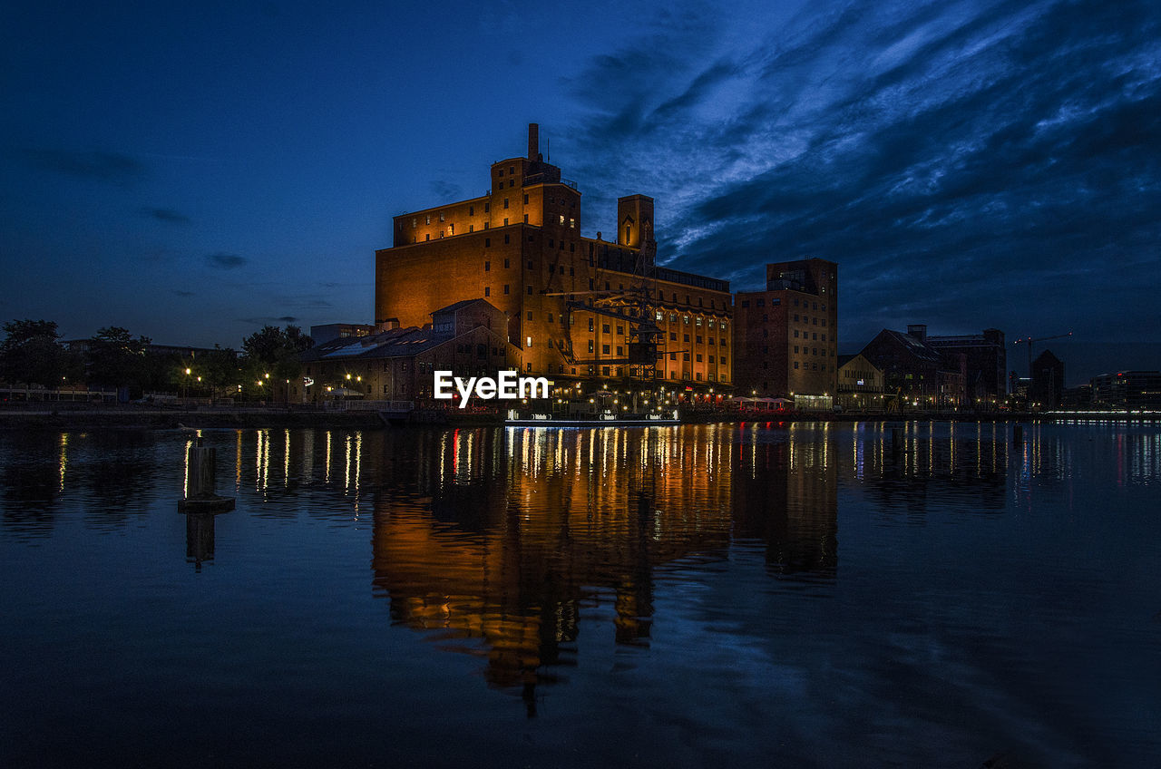 Illuminated buildings by lake against sky at night