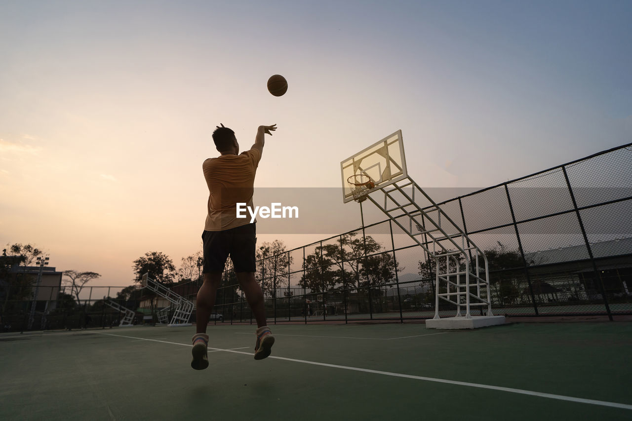 Man playing with ball against sky during sunset