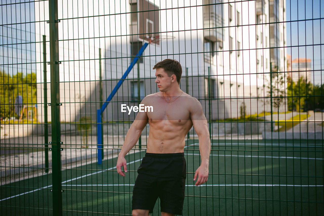 Muscular man standing against fence at park