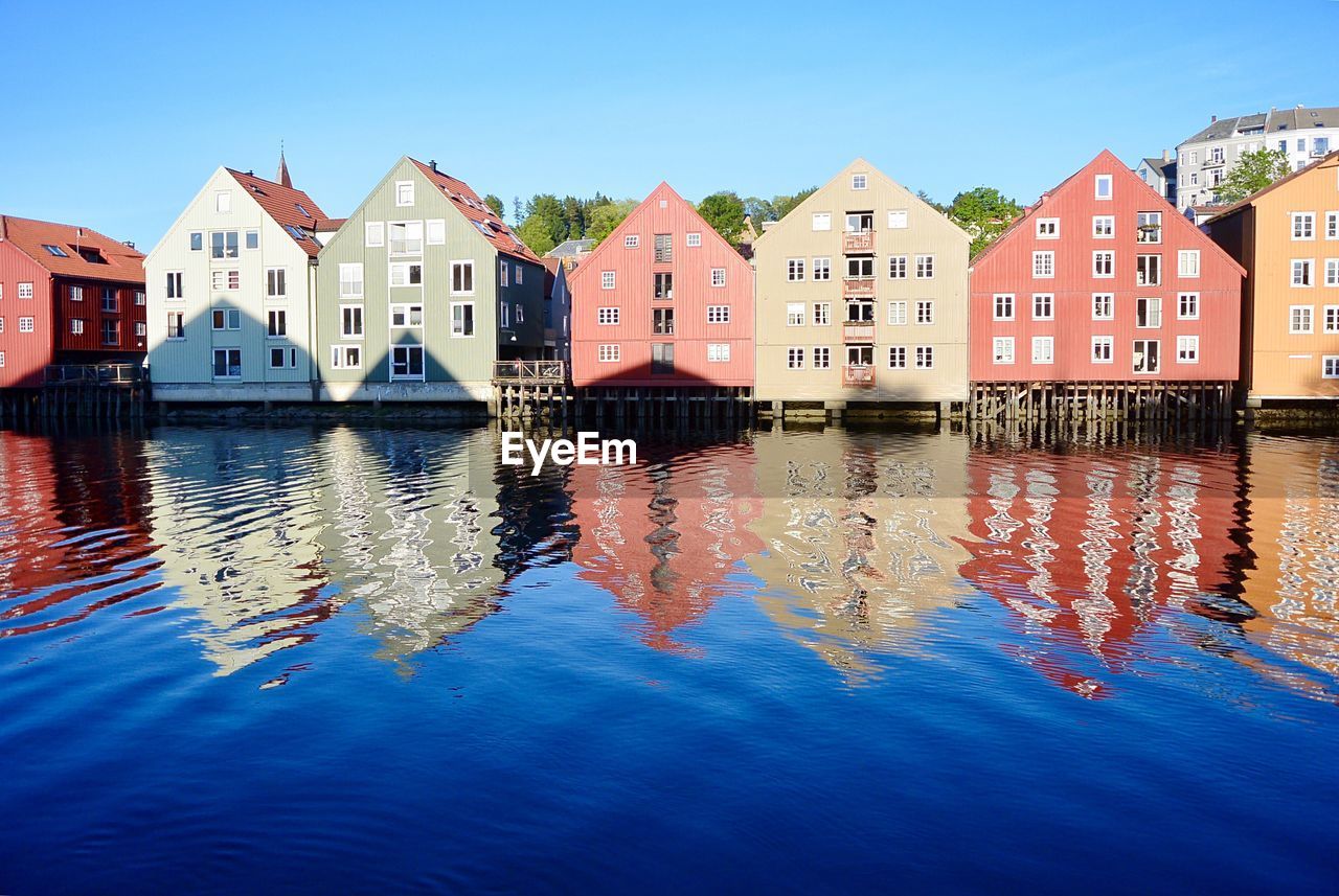 Buildings by river against blue sky