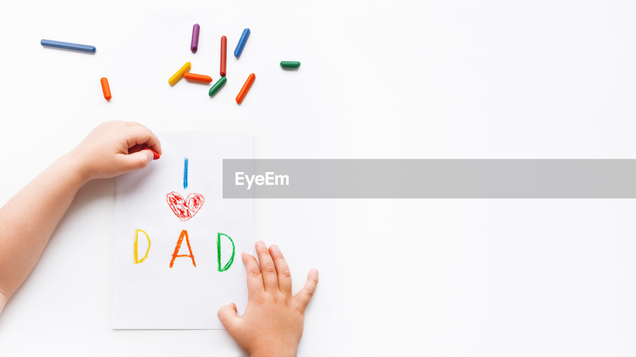 Left-handed toddler draws greeting card for father day - i love dad and to paint red heart symbol.