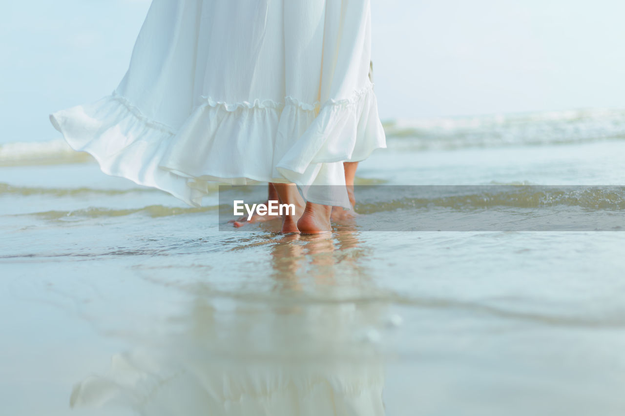 Low section of woman with umbrella on sea shore