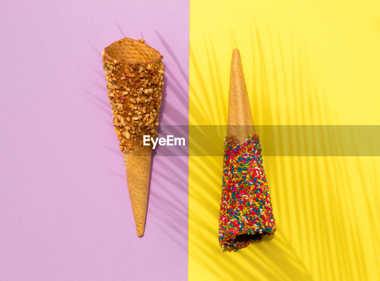 Colorful ice cream waffle cones and palm leaf shadow on pastel purple and yellow background. flat la