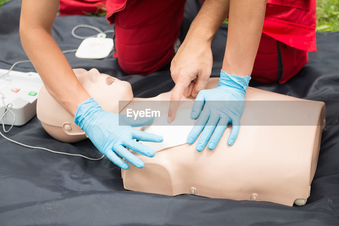 Cropped hand of man instructing while paramedic practicing cpr on dummy