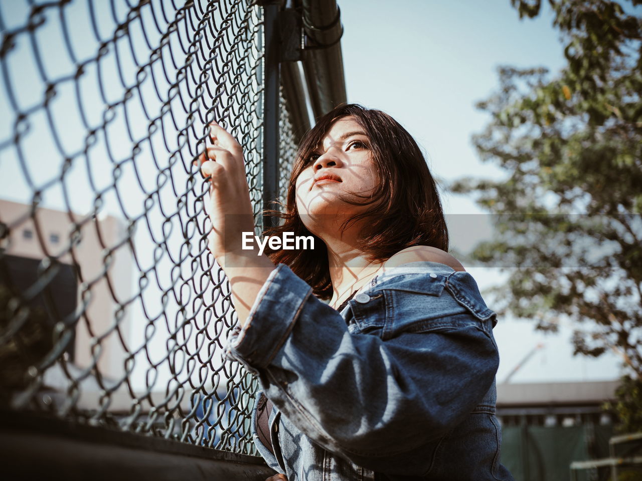 Low angle view of woman looking through chainlink fence