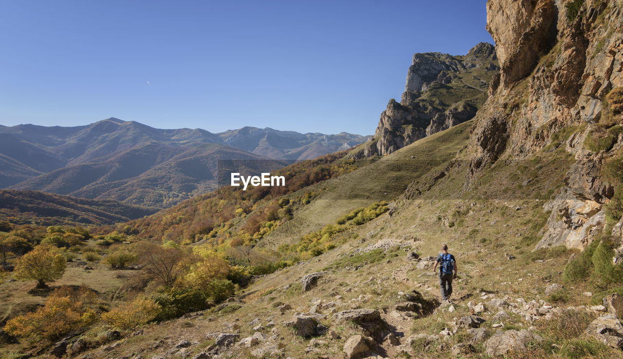 Rear view of hiker walking on mountain against sky