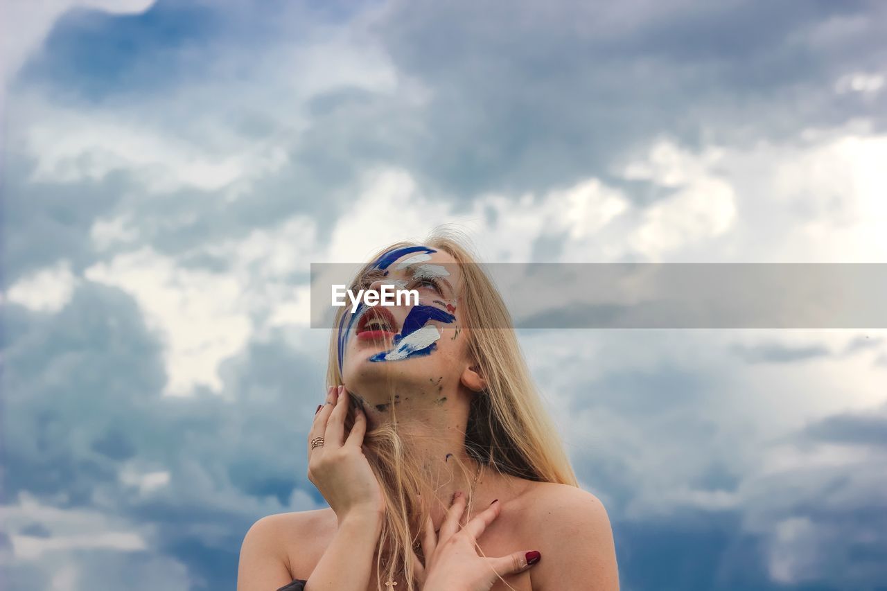 Young woman with face paint against cloudy sky