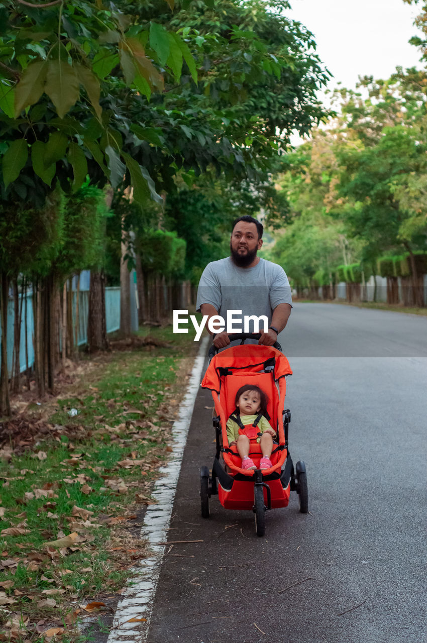 Portrait of man pushing stroller on the road.