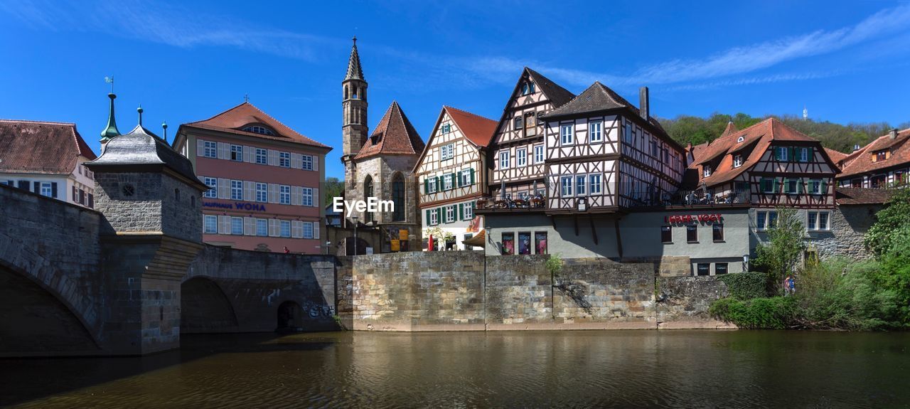 Buildings by river against blue sky