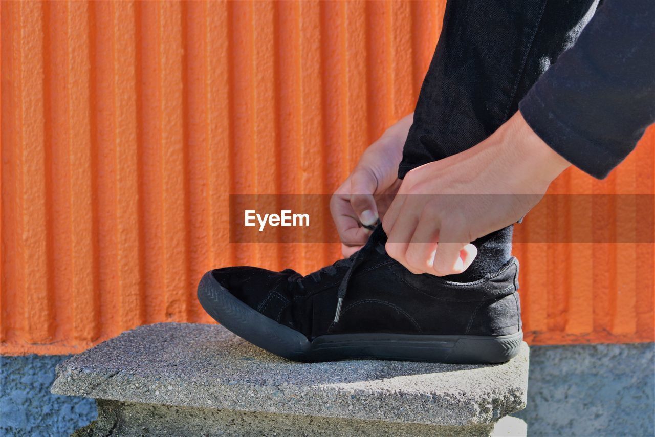 Low section of man tying shoelace on rock against orange wall