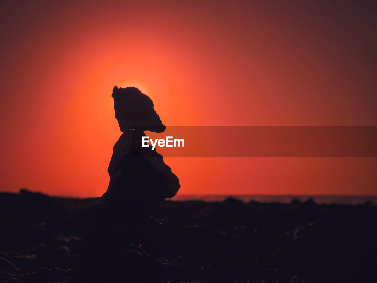 SILHOUETTE OF PERSON STANDING ON ROCK DURING SUNSET