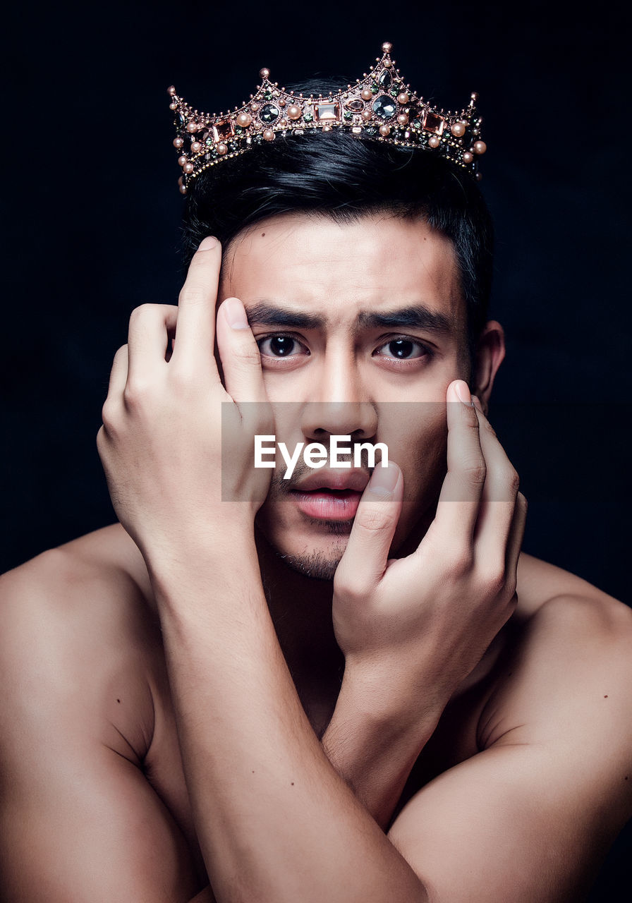 Close-up portrait of young man wearing crown against black background