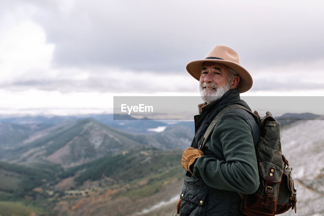 Side view of elderly male traveler with backpack standing in highlands in winter and admiring scenic landscape in caceres