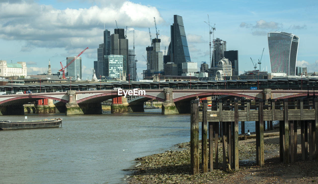 Bridge over river by buildings against sky in city