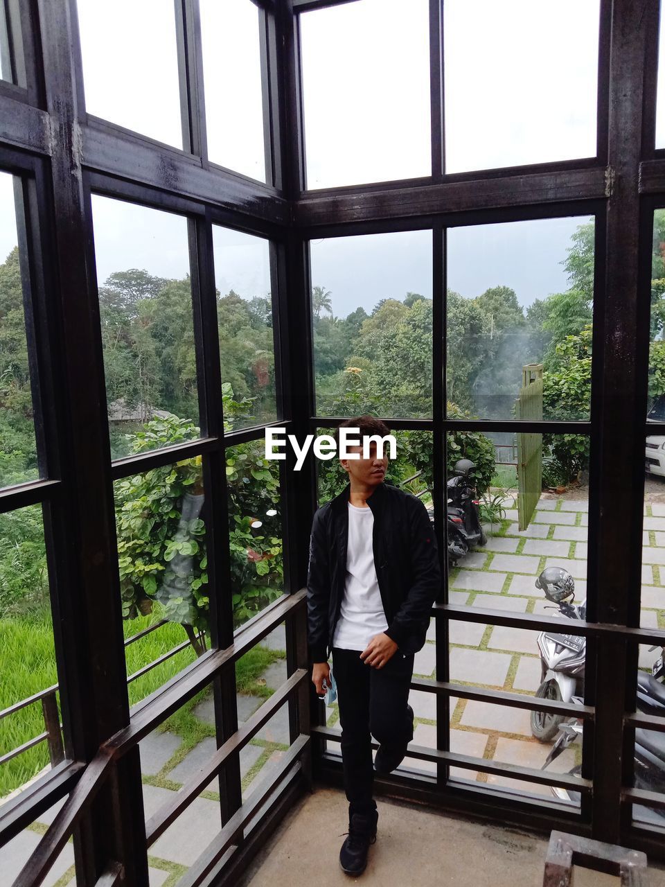 PORTRAIT OF YOUNG MAN STANDING AGAINST WINDOW