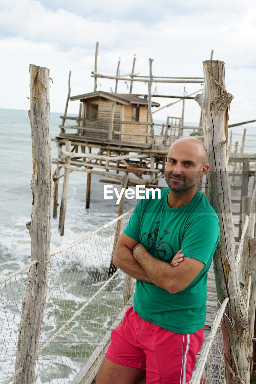 Portrait of bald man standing on pier over sea