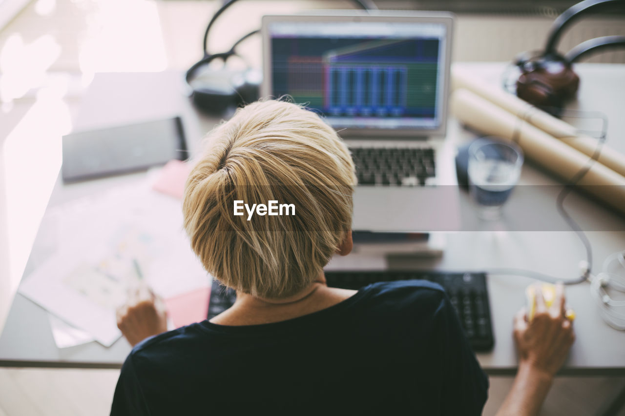 Rear view of woman working with laptop in office at home