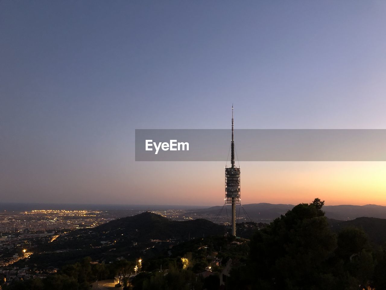 Communications tower in city against sky during sunset