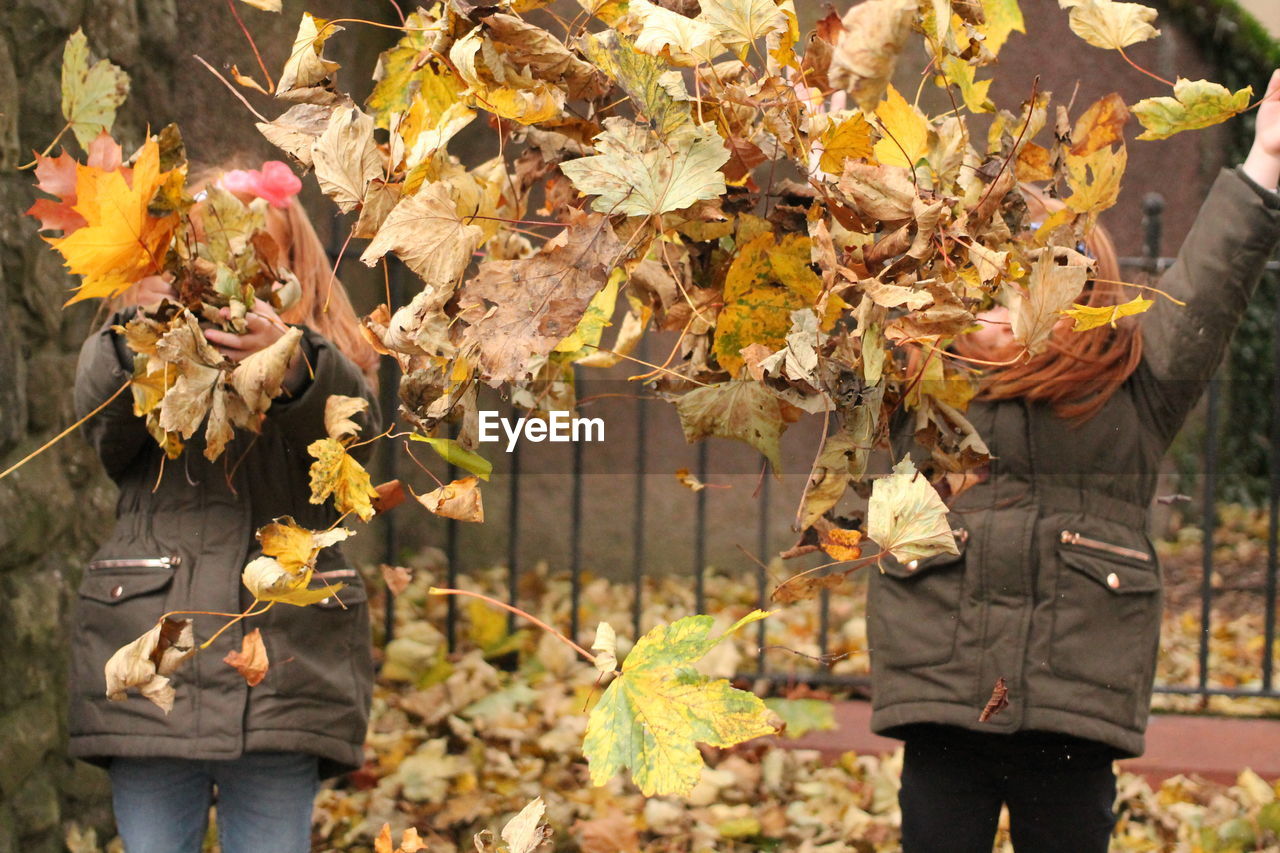  girls throwing dry leaves while standing outdoors 