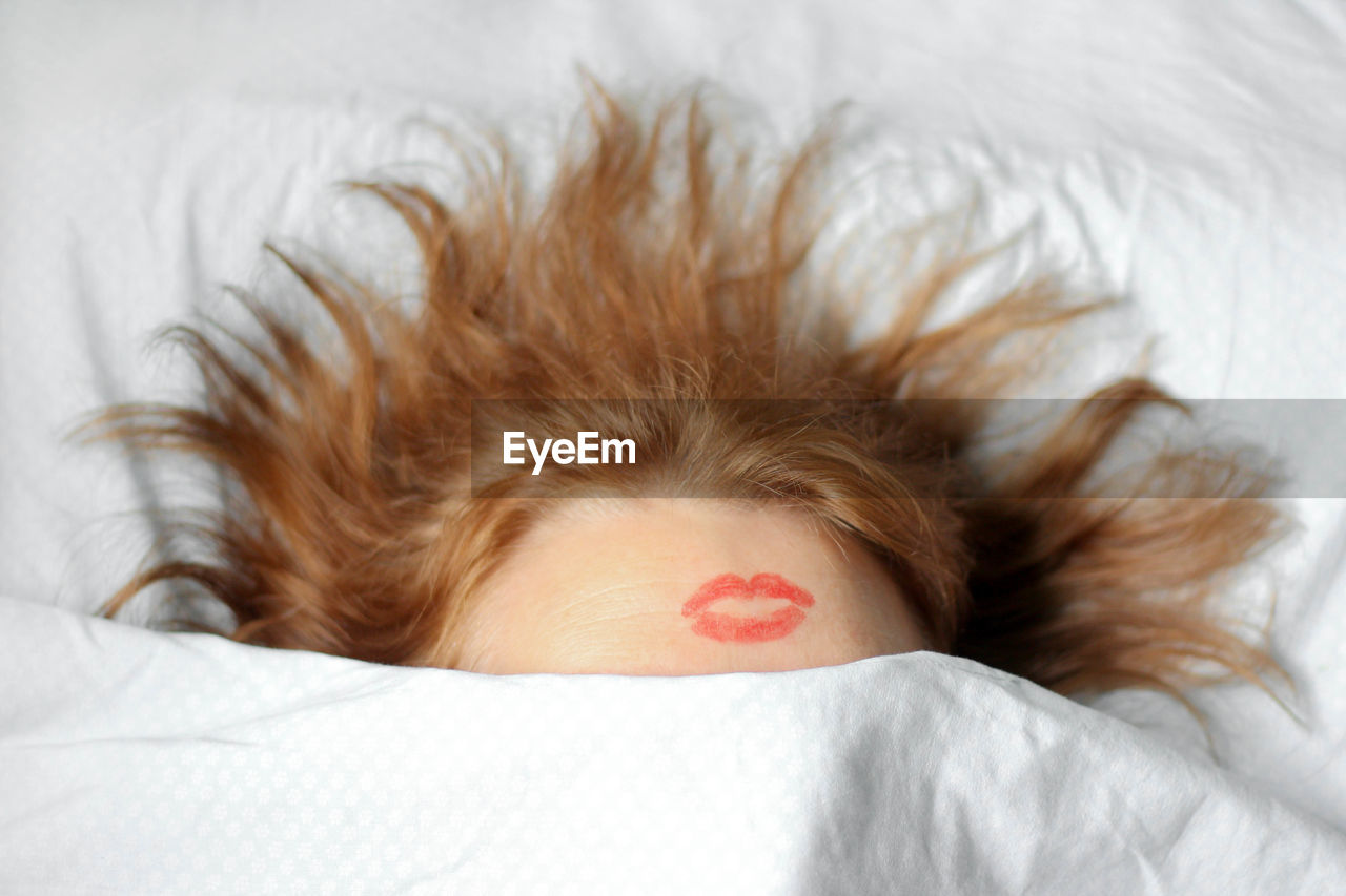 Woman with lipstick mark on head sleeping on bed