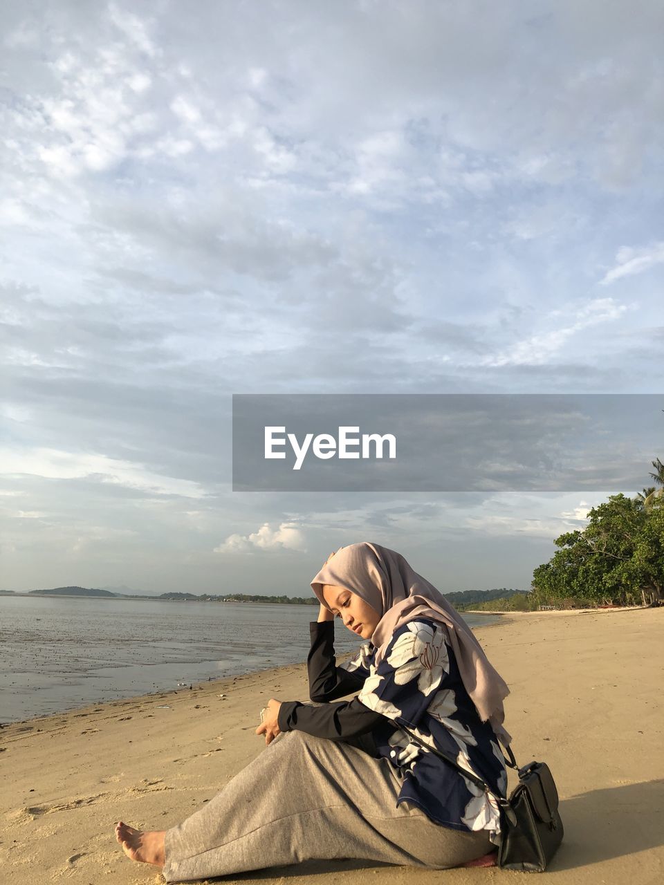 Woman sitting at beach against sky