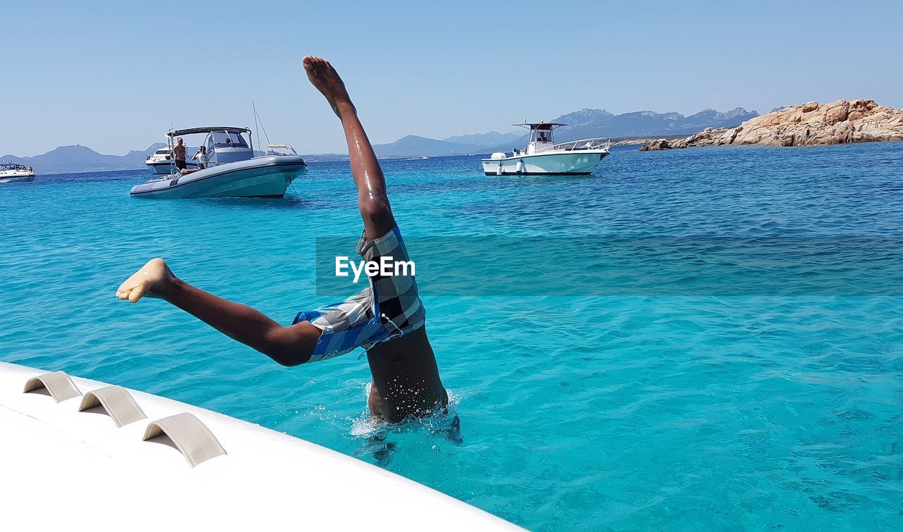 Shirtless man diving into sea from boat against clear sky