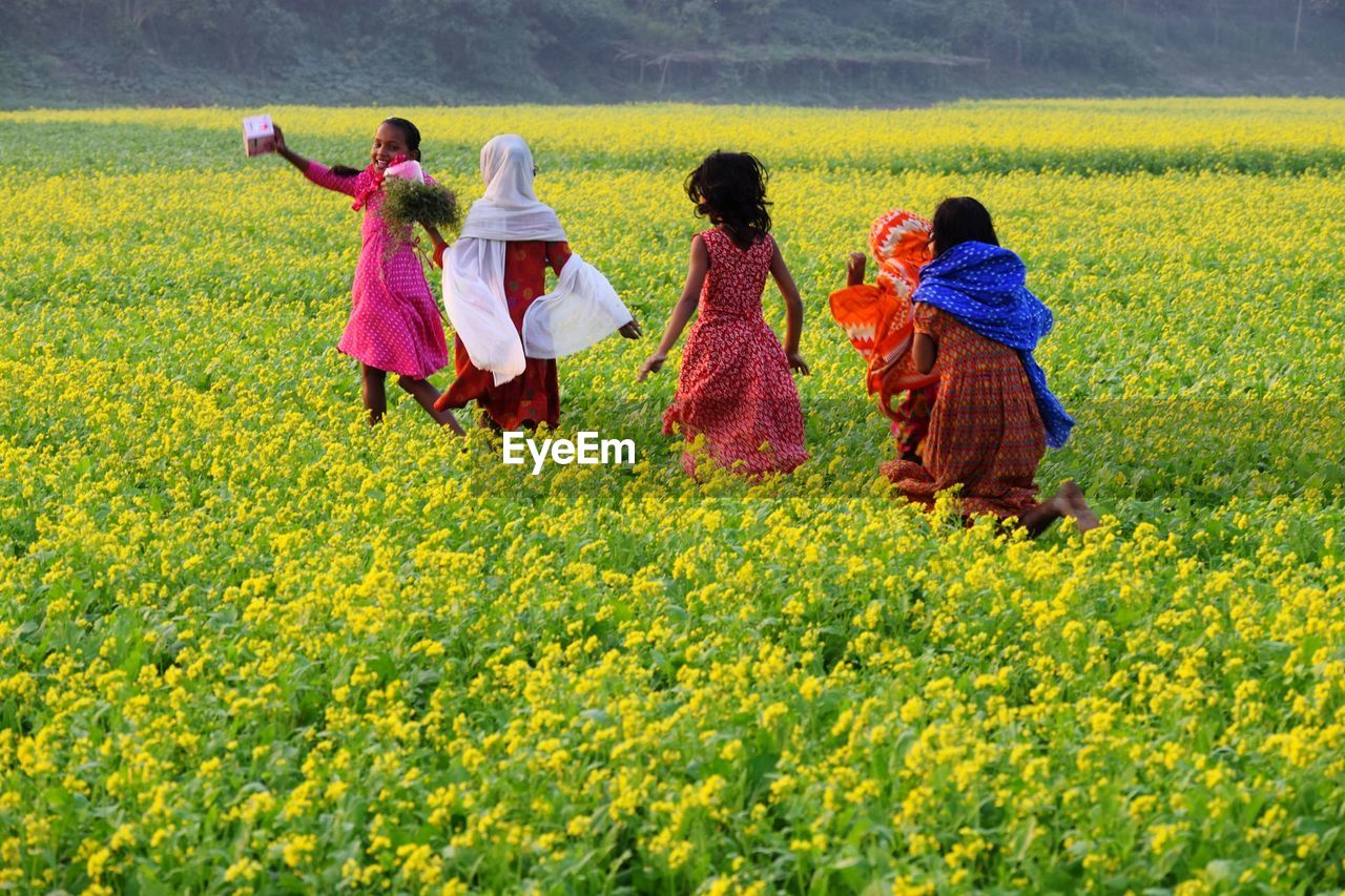 Girls amidst yellow flowers on field