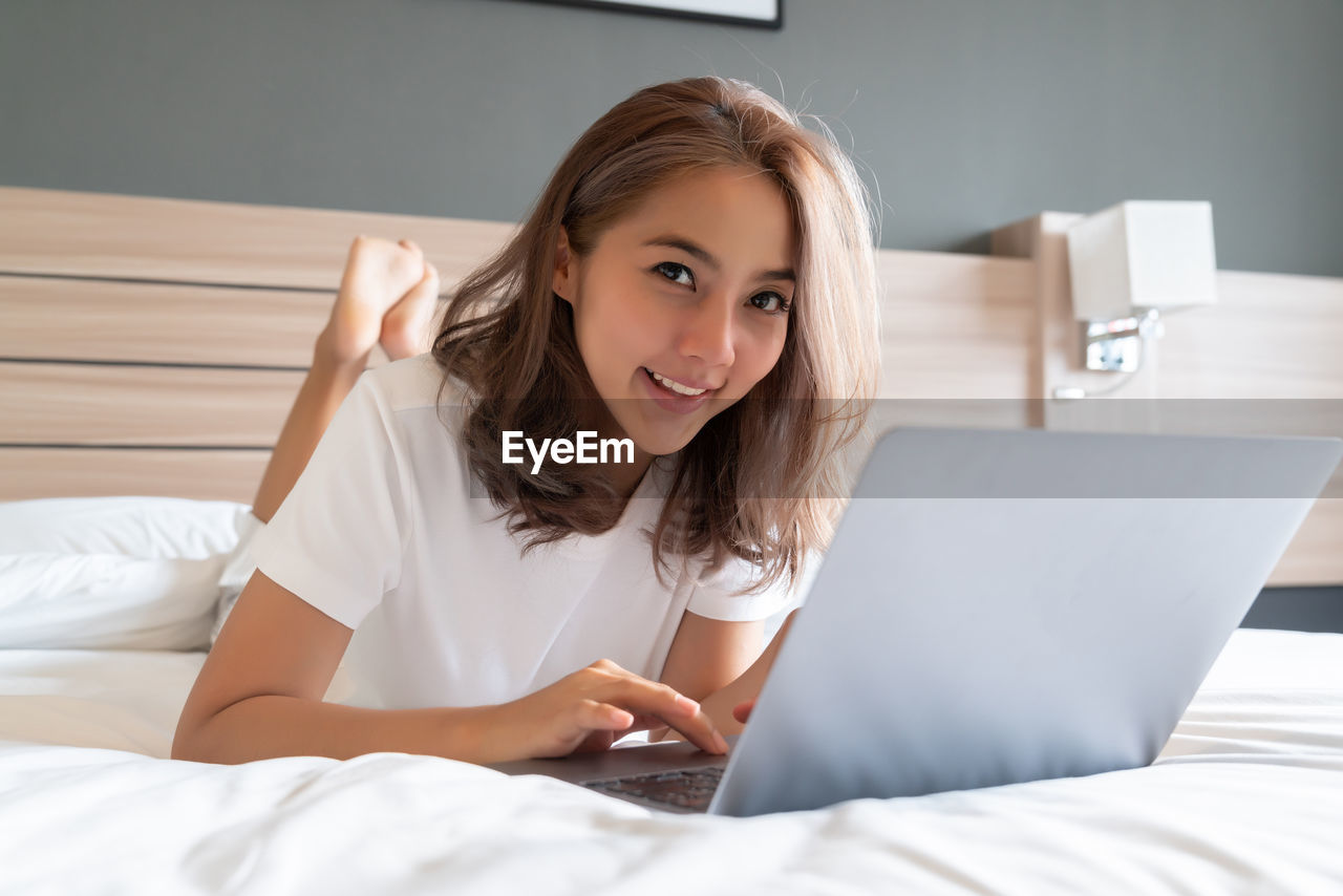 PORTRAIT OF A SMILING YOUNG WOMAN SITTING ON BED