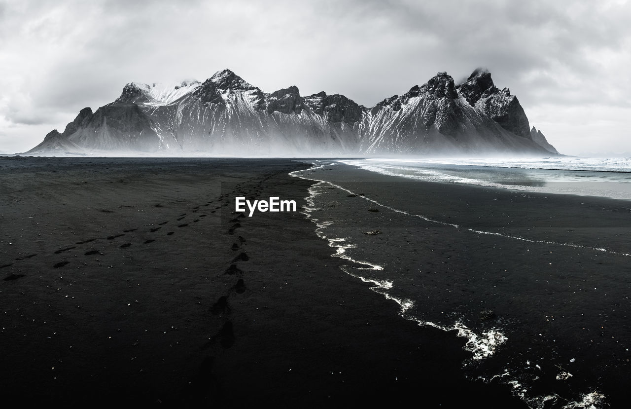 Scenic view of sea by snowcapped mountains against sky