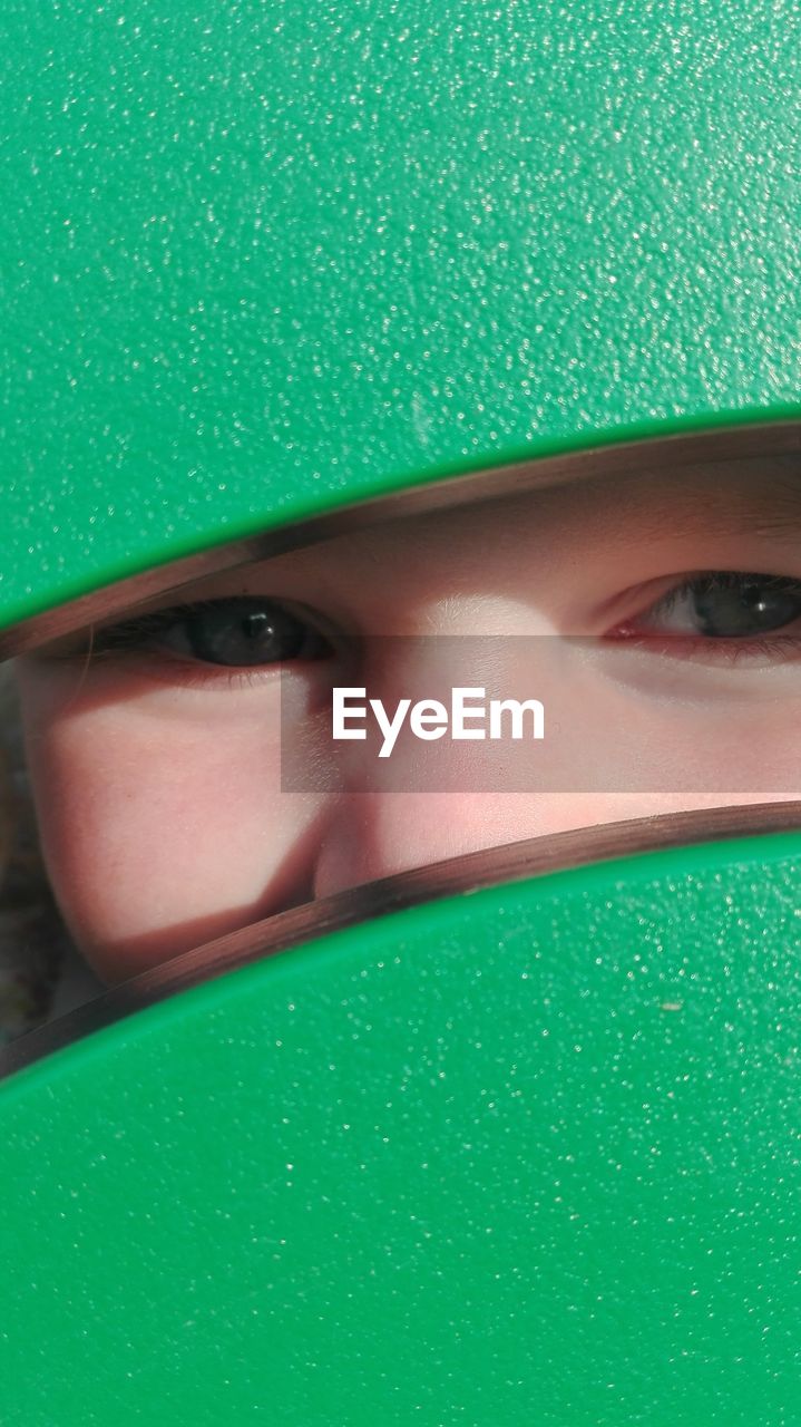 Close-up of girl hiding behind green play equipment at playground