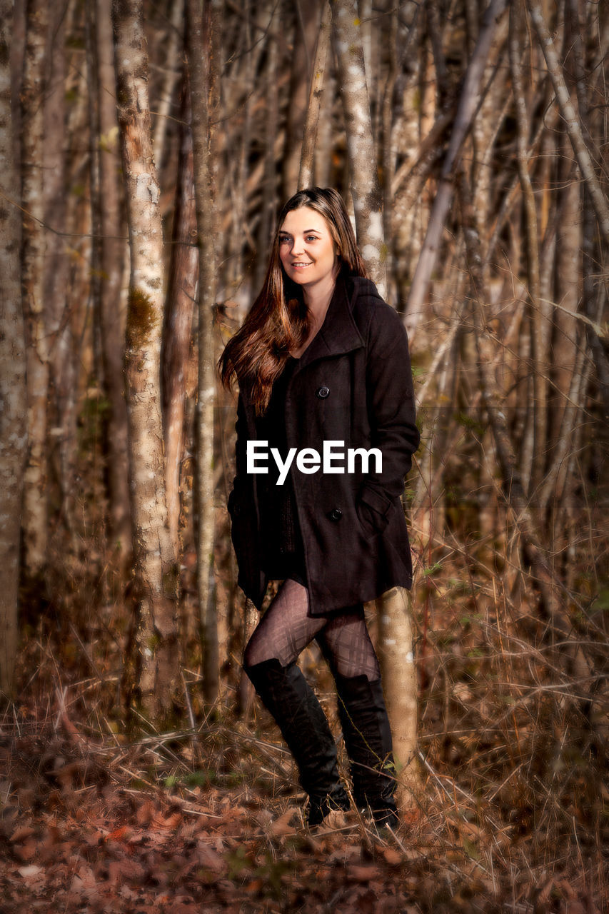 Young woman standing against trees in forest