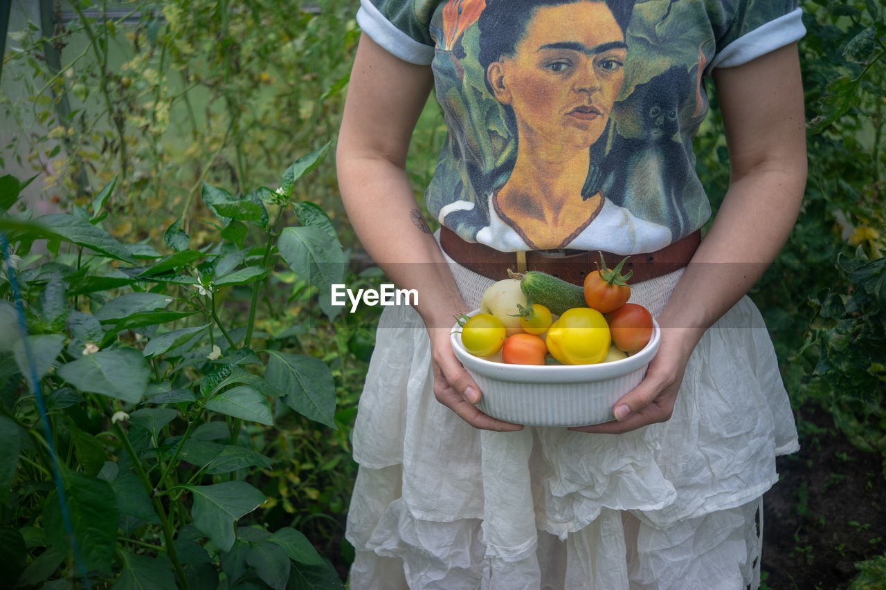 MIDSECTION OF WOMAN HOLDING FRUITS IN A FARM