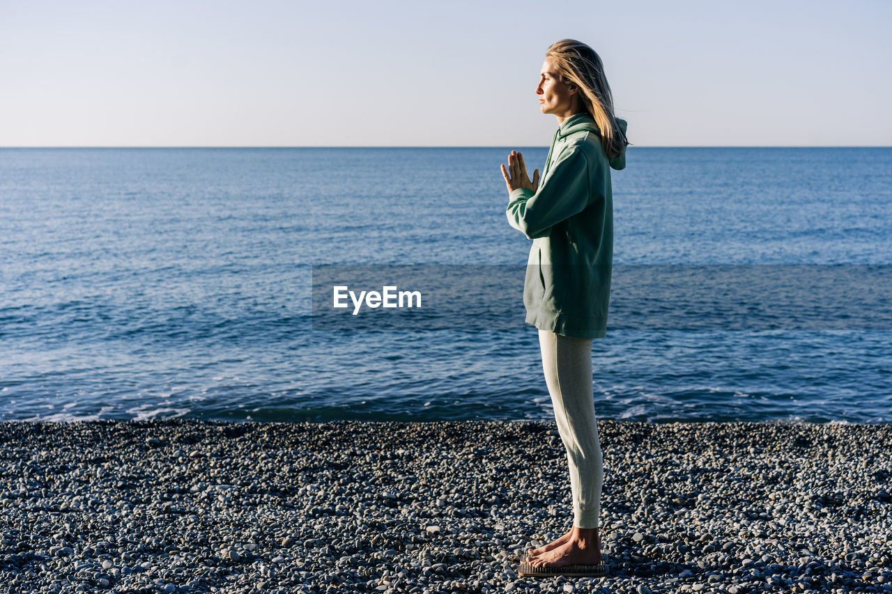 Woman on the seashore standing on boards with nails for yoga doing mental practice.