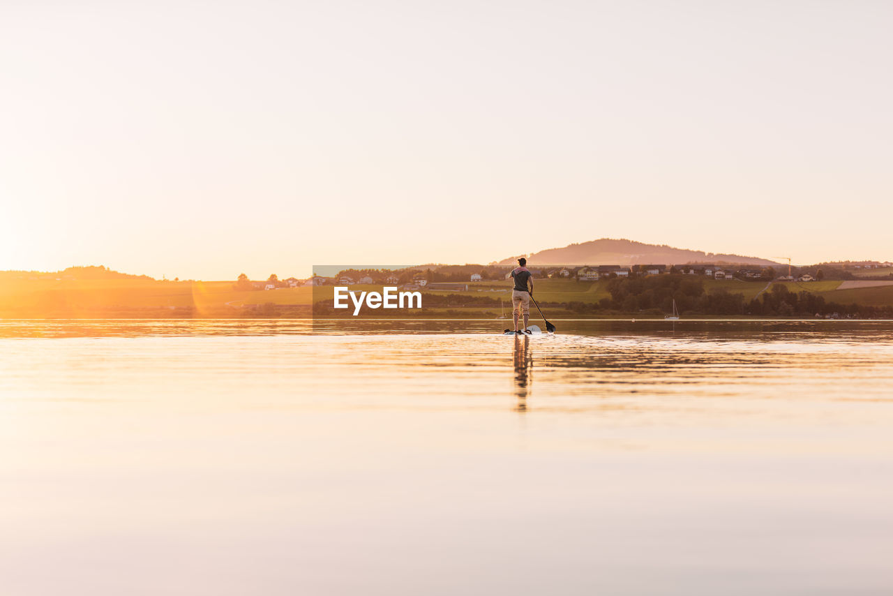 Young woman stand up paddling at sunset, lake wallersee, austria