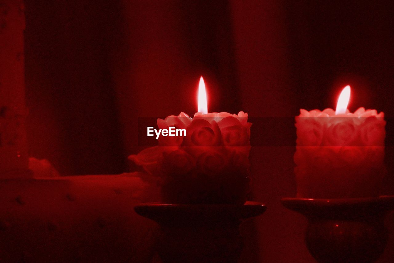 CLOSE-UP OF ILLUMINATED RED CANDLES IN DARKROOM