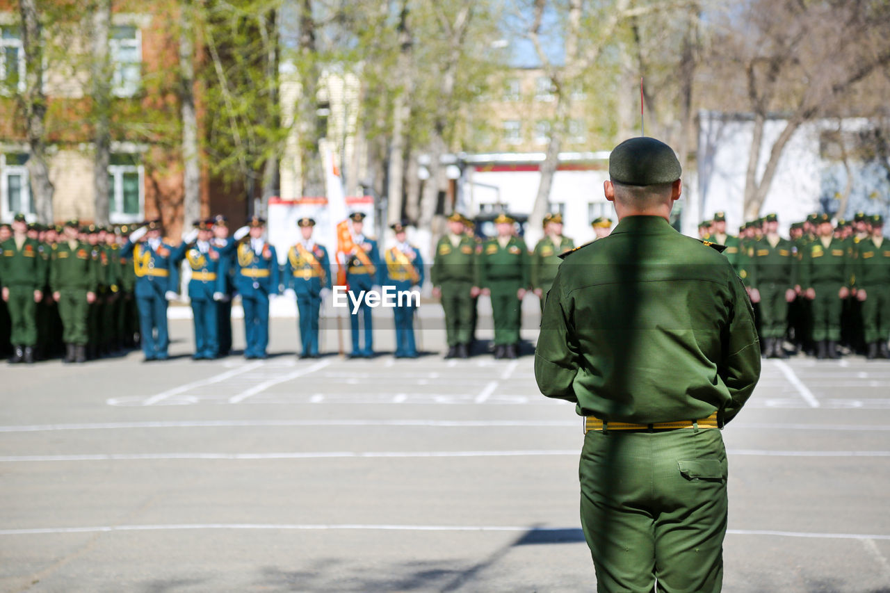 REAR VIEW OF PEOPLE STANDING ON STREET AGAINST CITY