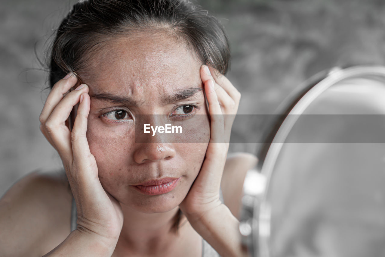 Close-up of woman with acne problem looking in mirror