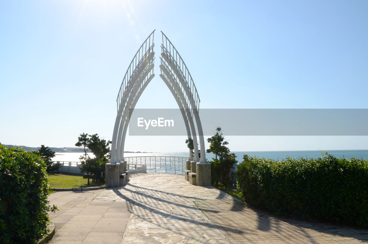 Walkway by sea against clear blue sky