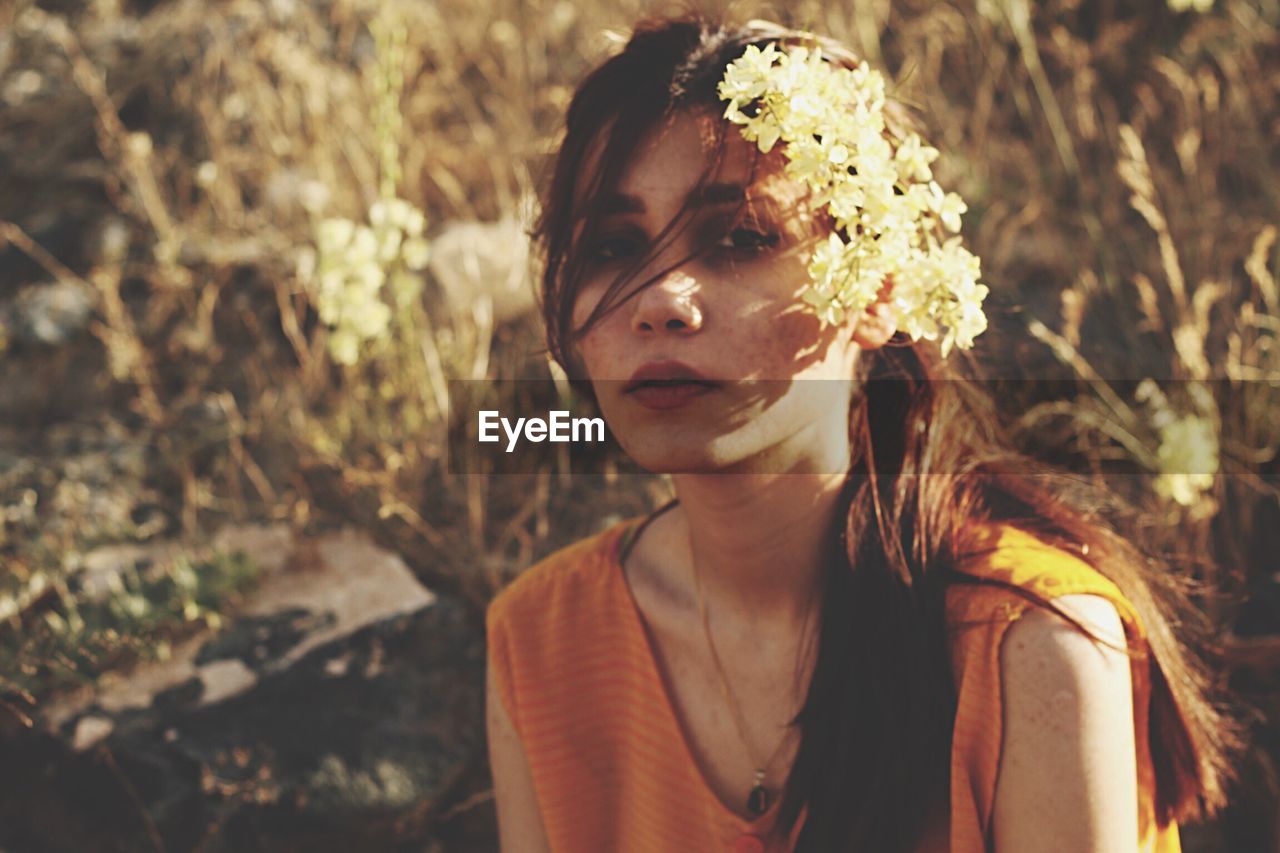 Portrait of young woman wearing flowers while sitting on field during sunset