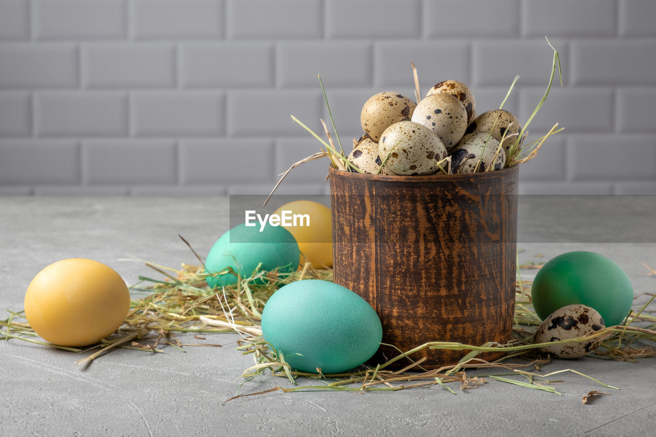 Easter composition from a clay vessel with quail eggs in hay surrounded by painted chicken eggs. 